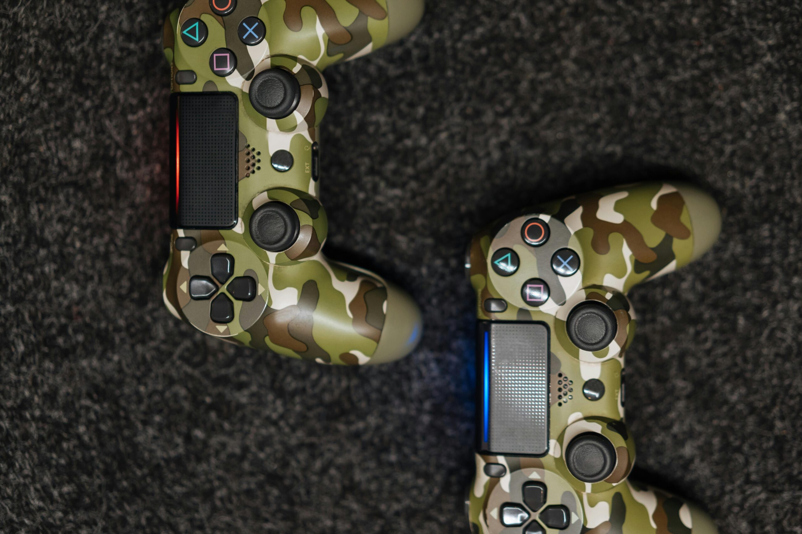 Close-up view of camouflage-patterned game controllers on a dark carpet background.