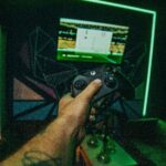 Unrecognizable tattooed male gamer with controller in hand playing video game in room with monitor and hookahs while spending time in modern club